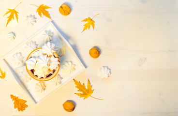 Autumn composition with a cup of meringues, yellow leaves, walnuts on a white wooden background