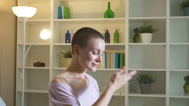 Woman meditating indoors. Attractive and short-haired caucasian model in white sportclothes sitting on mat and practice yoga with candles.