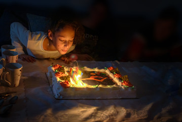 Adorable teen girl celebrating her birthday and blowing candles on beautiful Birthday chocolate cake, indoor. Birthday party for kids. Low key image.
