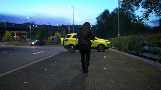 Woman walking to her car at night in a shopping area carpark, unlocking the car and dropping her keys on floor. Selective focus on the woman