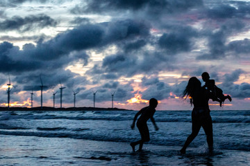 mother and sons sunset at the beach with wind mills on the back ground