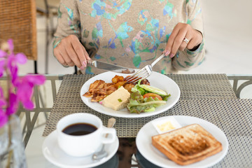 Woman holding knife and fork eating breakfast with slice of toast and coffee.