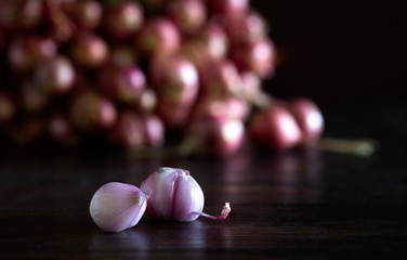 Bunch of shallot and some shallots fall off and peeled on dark wooden background which has dim light