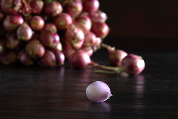 Bunch of shallot and some shallots fall off and peeled on dark wooden background which has dim...
