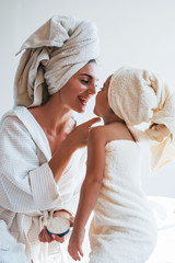 Using cream to clear skin. Young mother with her daugher have beauty day indoors in white room