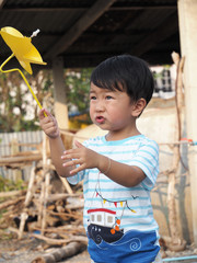 Asian lovely kid holding playing a yellow windmill toy with countryside background. Cute young boy learning how turbine blow. Freedom and happy time. Preschool learning concept.