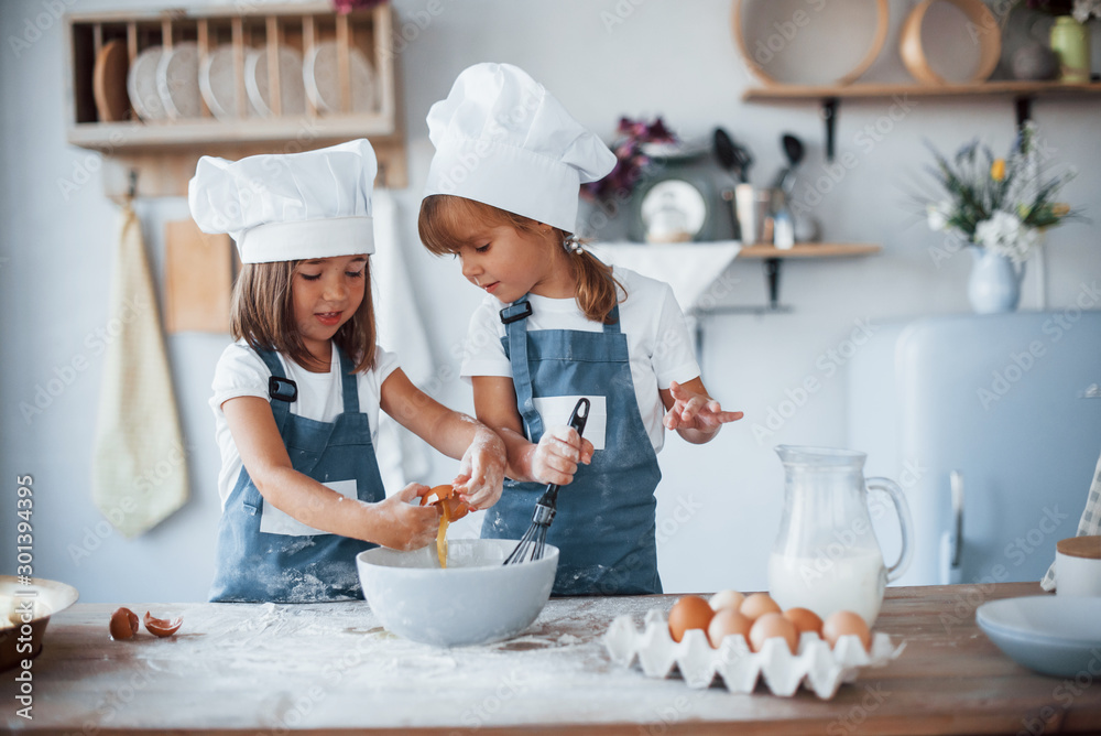 Wall mural family kids in white chef uniform preparing food on the kitchen