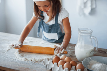 Cute kid in white chef uniform preparing food on the kitchen