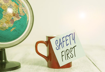 Conceptual hand writing showing Safety First. Concept meaning used to say that the most important thing is to be safe Globe map coffee cup sticky note lying vintage wooden table