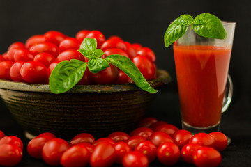 CHERY TOMATOES ON BLACK BACKGROUND WITH BASIL AND JUICE WITH SELECTIVE FOCUS