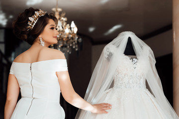 Attractive bride in white dress, touches the wedding dress on the mannequin in wedding morning. Trendy wedding style shot. Sexy bride. Bride touch your white wedding dress. Fashion bride