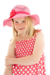 Close up of smiling beautiful young blonde girl wearing big pink floppy hat and a polka dot dress. Isolated on white studio background