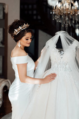 Attractive bride in white dress, touches the wedding dress on the mannequin in wedding morning. Trendy wedding style shot. Sexy bride. Bride touch your white wedding dress. Fashion bride
