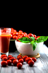 CHERY TOMATOES ON BLACK BACKGROUND WITH BASIL AND JUICE WITH SELECTIVE FOCUS