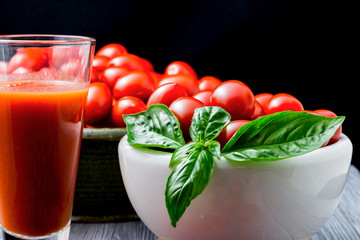 CHERY TOMATOES ON BLACK BACKGROUND WITH BASIL AND JUICE WITH SELECTIVE FOCUS