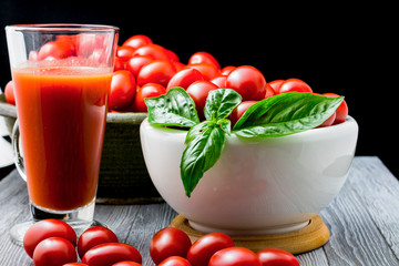 CHERY TOMATOES ON BLACK BACKGROUND WITH BASIL AND JUICE WITH SELECTIVE FOCUS