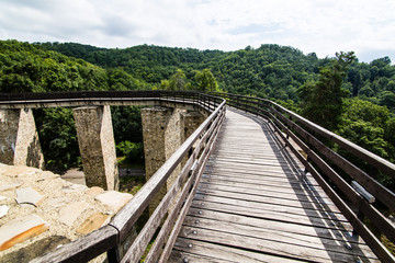 Fototapeta na wymiar Wooden bridge held by massive rock pillars leads the way into the Neamt Citadel is a medieval fortress located in north-eastern part of Romania, near Targu Neamt, Neamt County.