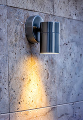 Metal design outdoor spotlight lamp lights on a tiled wall.