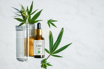 Glass bottle with cannabis oil with label and a test tube with hemp leaves on a marble background....