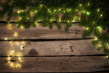 Green Christmas tree branches with lights on rough weathered wooden planks