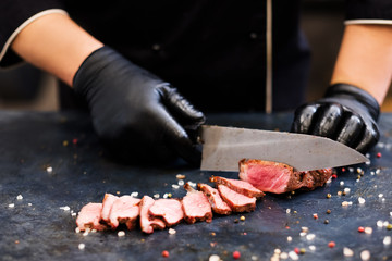 Culinary master class. Striploin steak. Closeup of chef hands slicing medium rare grilled beef meat.