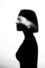 Fashionable beauty portrait. Black silhouette on white background. Girl with a spot of light on her face. 