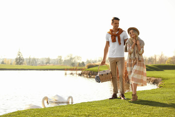 Obraz premium Young couple with picnic basket near lake on sunny day