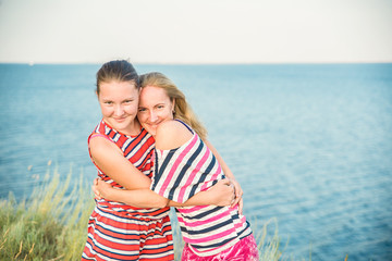 Fototapeta na wymiar Blonde mother and teenage daughter, dressed in striped clothes, hug and laugh on a sunny summer day on the lake.