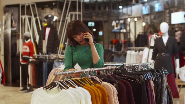 Nice woman choses a sweater and talks on the phone rapturously