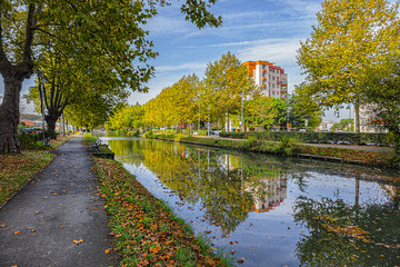 Fototapeta na wymiar Beautiful autumn views of Canal du Midi (in XVII century - Royal Canal in Languedoc) in Toulouse and trees reflection in water. Toulouse, Haute-Garonne, France.