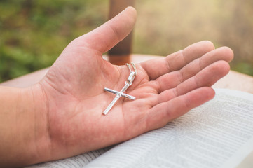 Woman holding a the cross in hand against the background of the bible. 