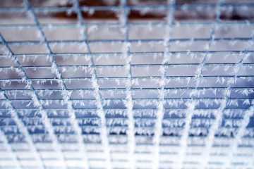 The grid on a frosty day is covered with frost in cold colors
