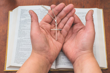 Woman holding a the cross in hand against the background of the bible. 