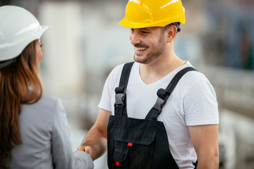 Architect and worker working on project. Colleagues handshaking in factory.