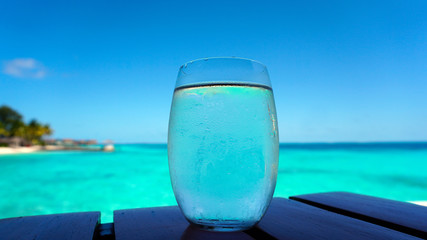 Clear glass water cocktail with blue turquoise ocean background