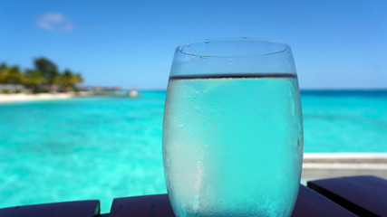 Fototapeta na wymiar Clear glass water cocktail with blue turquoise ocean background