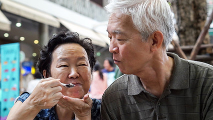 Loving Asian elder couple feeding ice crean happy dating outdoor