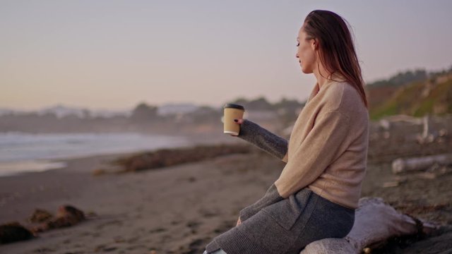 Woman enjoying hot drink on a sunset near ocean