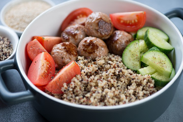 Close-up of a serving pan with quinoa, fried meatballs and fresh vegetables, selective focus, studio shot