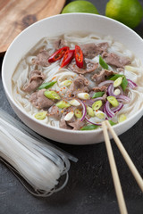White bowl with traditional vietnamese pho bo soup, vertical shot, close-up