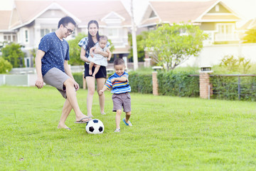 Portrait of Asian family playing football together in garden