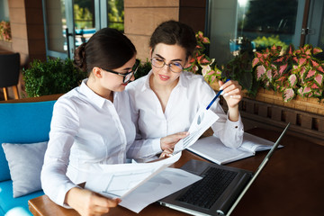 Happy beautiful young businesswomen or students working on laptop in street cafe outdoor