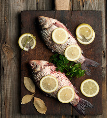 fresh crucian fish sprinkled with spices and lemon slices and lies on a brown wooden cutting board