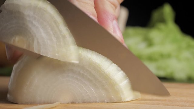 Cutting onions on dark wooden table with large kitchen knife. Slow motion view