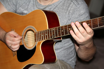 Fototapeta na wymiar man plays a six-stringed wooden guitar, musical concept, close-up