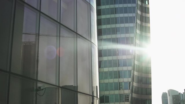 Beautiful lens flare through Skyscrapers with green and blue glass windows at business district in Paris, Side track to right then left, wide shot with reflections. Futuristic modern building.