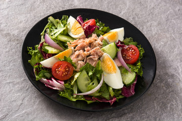 Salad with tuna, egg and vegetables on black plate and gray background