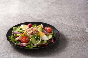 Salad with tuna, egg and vegetables on black plate and gray background. Copy space