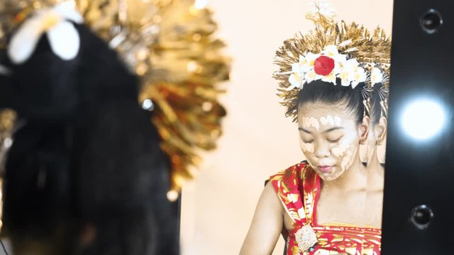Balinese dancer applying cosmetic foundation on her face in front of a mirror in makeup room. Shot in 4k resolution