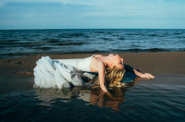 Portrait of young blond bride lies on sand among the water